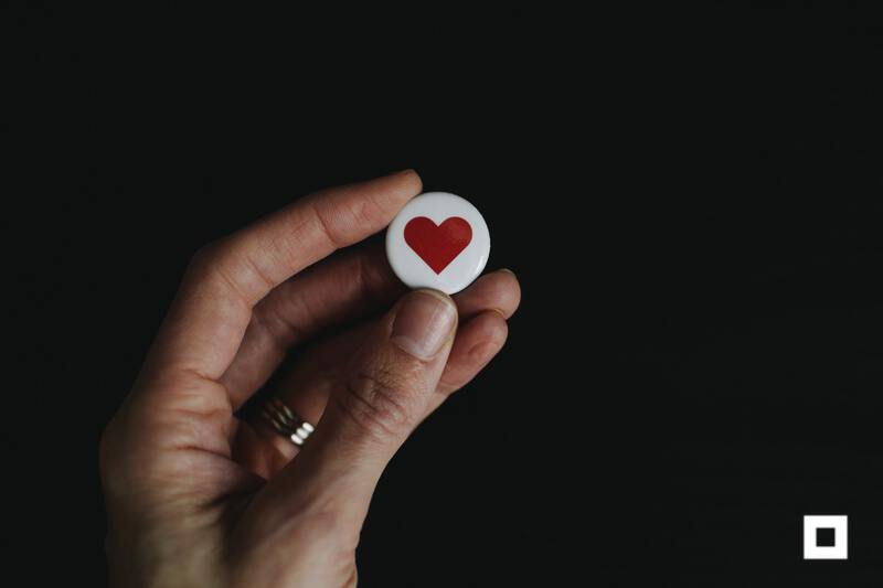 Hand holding button with heart painted on it